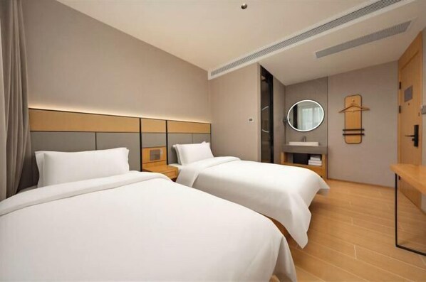 A hotel room with two beds, a bedside table, a mirror, a coat rack, and a wooden floor.