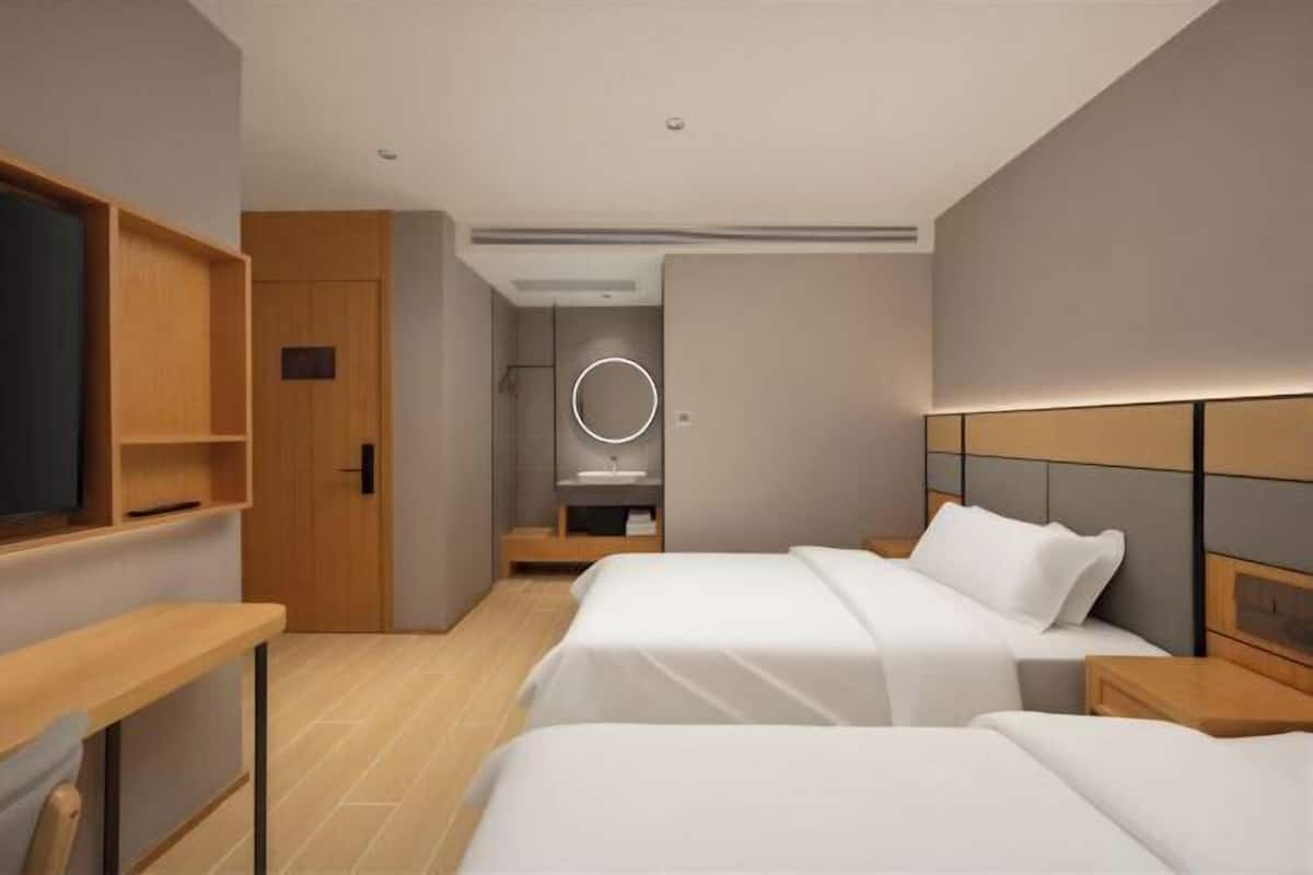 Quarto de hotel moderno com duas camas, uma escrivaninha, televisão e banheiro com espelho.