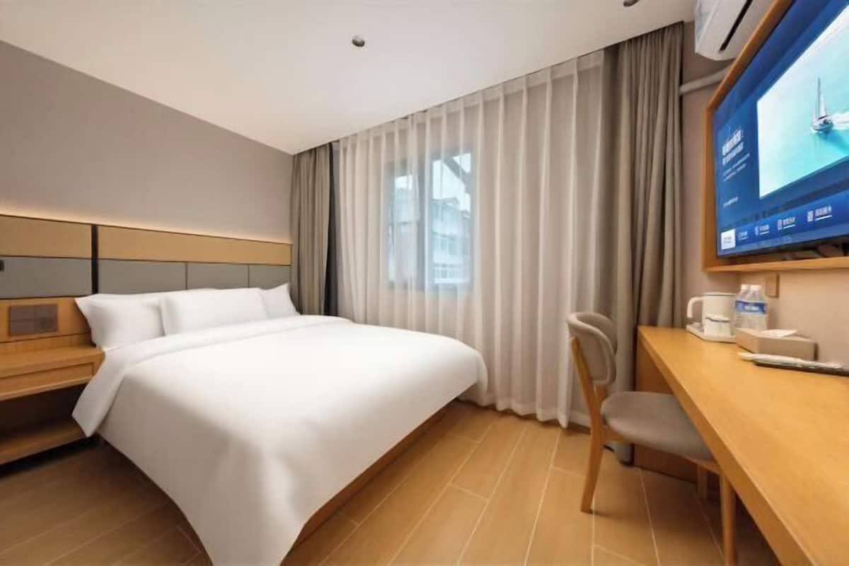 Quarto de hotel com cama, escrivaninha, cadeira, televisão e janela com cortinas.