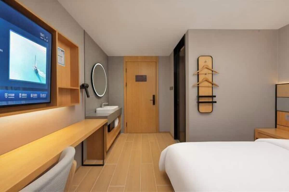 Quarto de hotel com cama, escrivaninha com monitor de computador, pia e espelho.