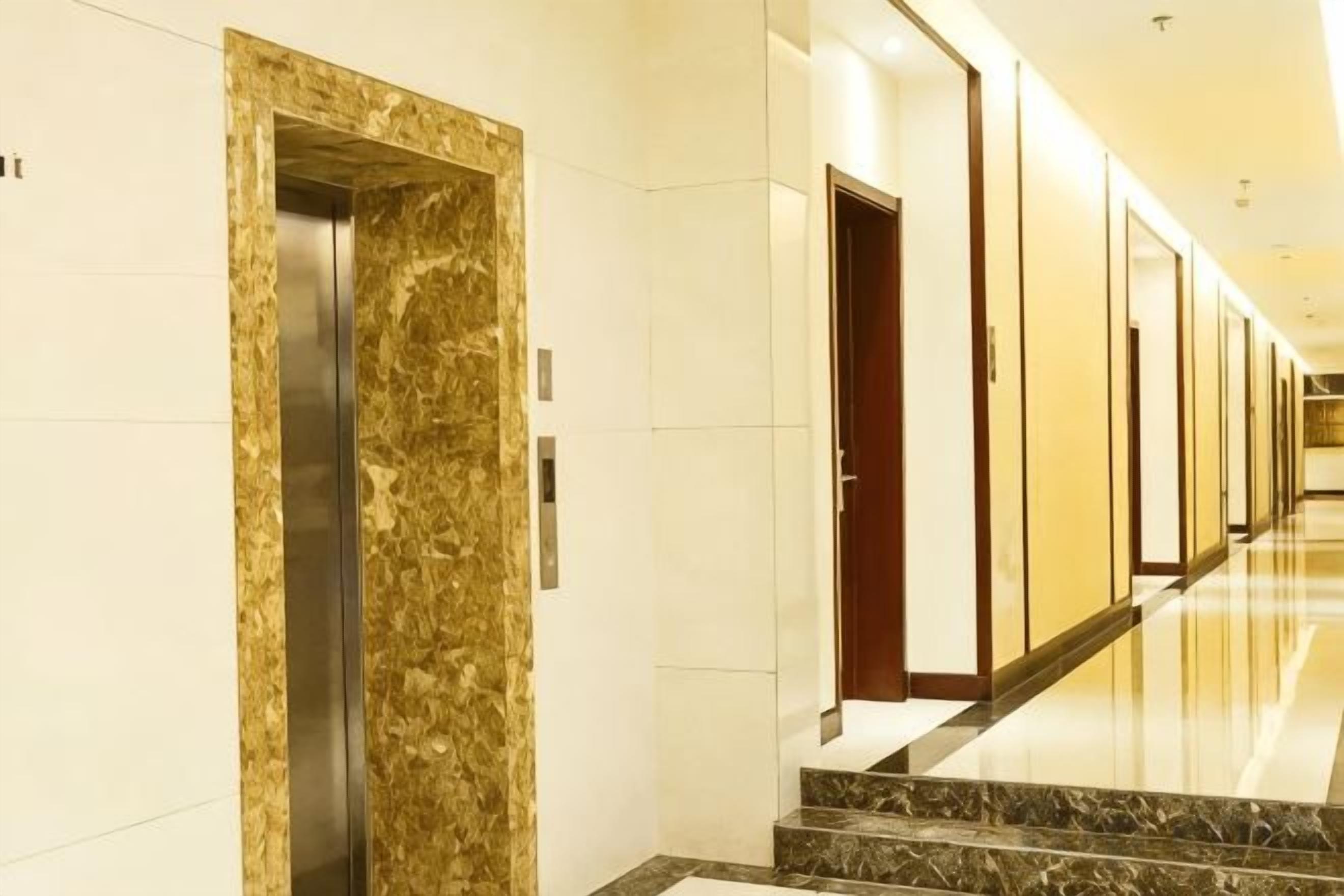 A hotel corridor with a marble elevator, doors, and a polished floor.