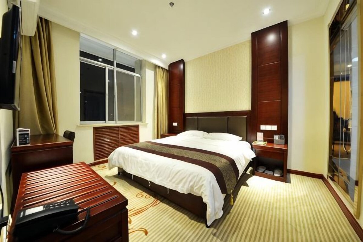 A hotel room with a large bed, a desk, a chair, a suitcase, and a window.