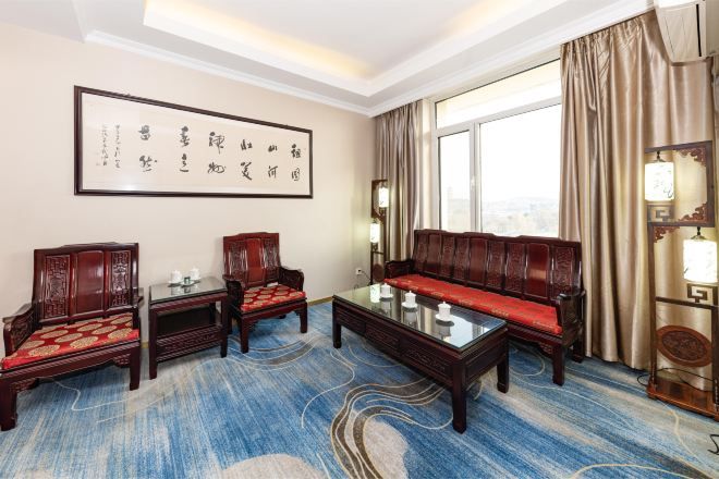 A traditional room with a sofa, two chairs, a coffee table, and a large framed calligraphy piece on the wall.