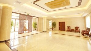A spacious lobby with a polished floor, a large pillar, wooden doors, and a seating area with chairs. - Taixi Hotel (Feicheng)