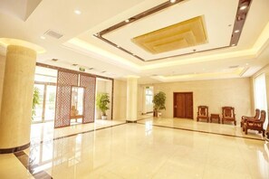 A spacious lobby with a polished floor, a large pillar, wooden doors, and a seating area with chairs.