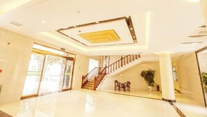A spacious lobby with a polished floor, a staircase, and a seating area with a potted plant. - Taixi Hotel (Feicheng)