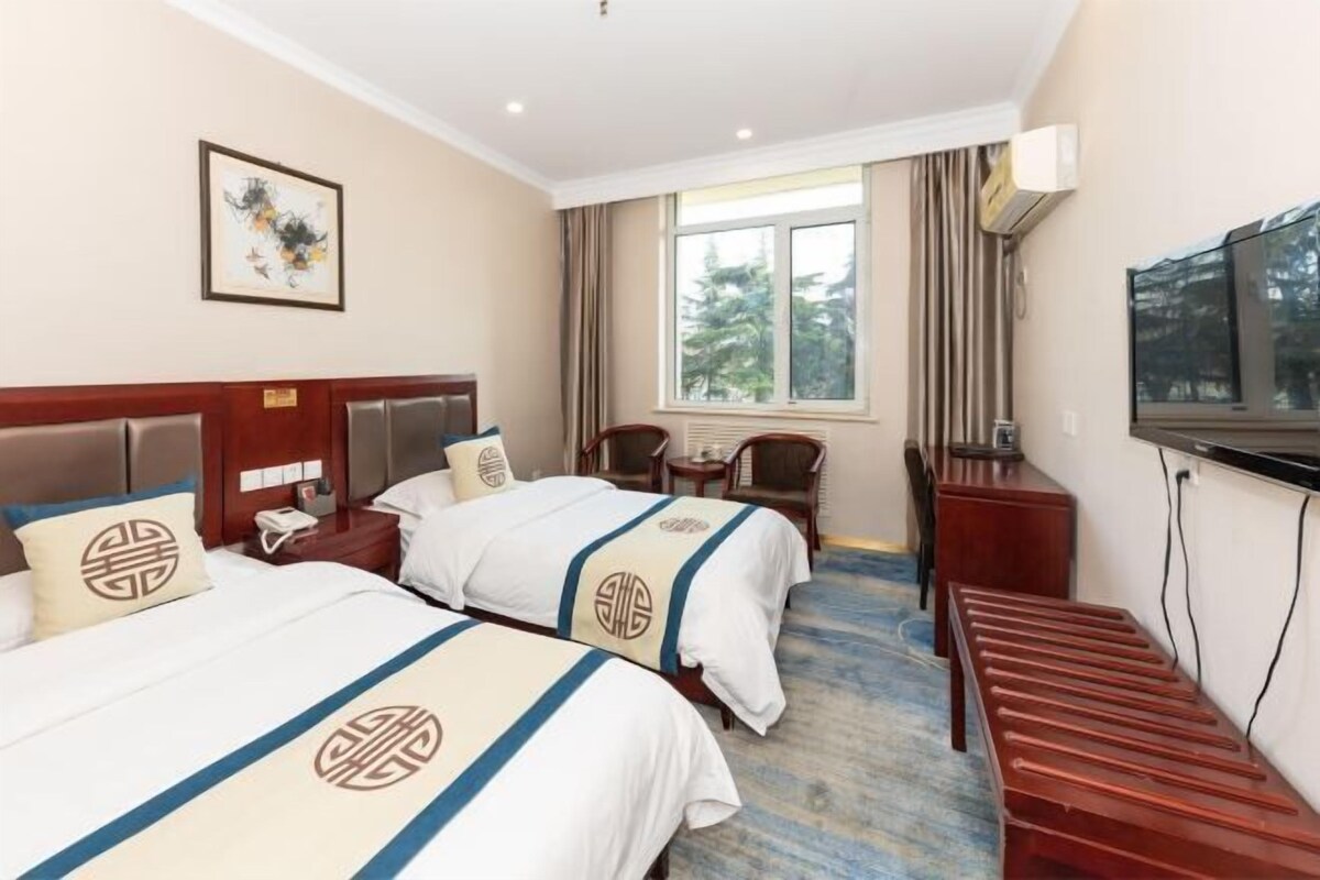 A hotel room with two beds, a desk, a chair, a TV, and a window with curtains.
