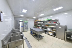 A commercial kitchen with stainless steel appliances, a sink, and storage shelves. - Taixi Hotel (Feicheng)
