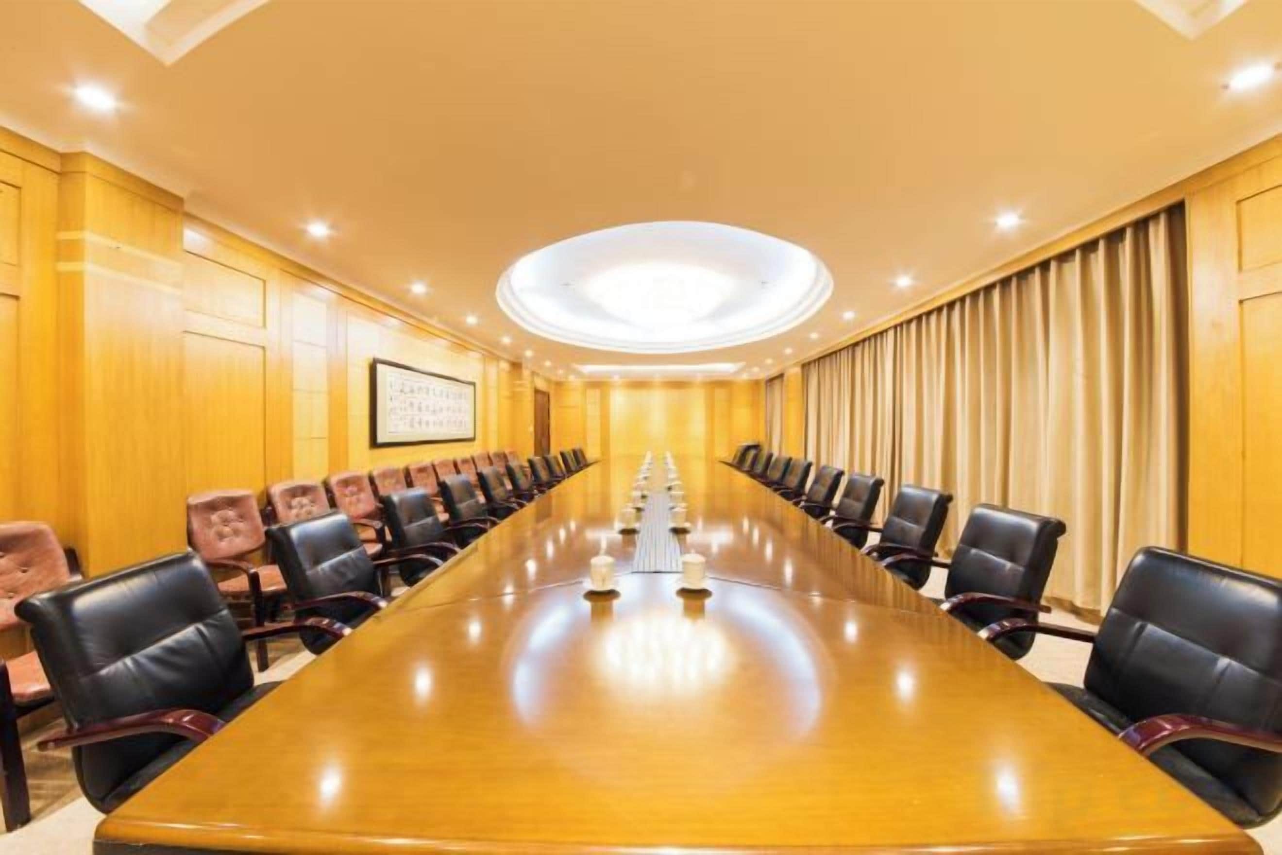 Une salle de conférence avec une longue table et des chaises, des murs en bois et un luminaire au plafond.