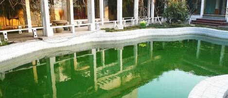 Una piscina con borde de azulejos, rodeada por una estructura blanca con columnas y una zona cubierta.