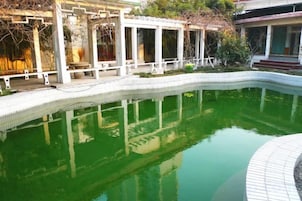 Una piscina con borde de azulejos, rodeada por una estructura blanca con columnas y una zona cubierta.
