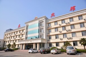 A multi-story hotel with a central entrance, parking area, and several cars parked in front.