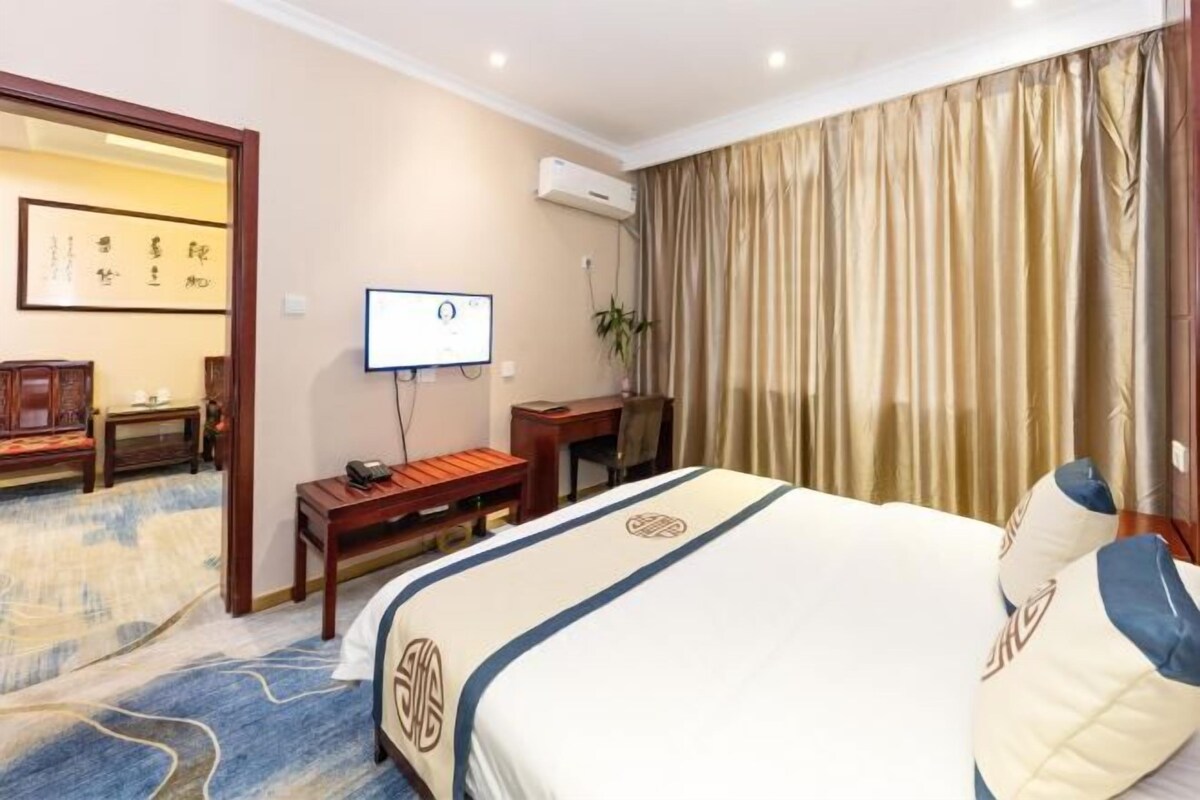 A hotel room with a bed, a desk, a chair, a television, and a curtain.