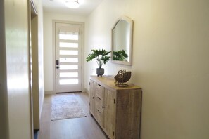 A hallway with a wooden cabinet, a potted plant, and a mirror on the wall. - Red Rock Oasis.  All Brand New furnishings and Soft Water! (Santa Clara)