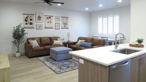 Una sala de estar moderna con un sofá de cuero marrón, un reposapiés azul, una mesa de centro de madera y una planta en maceta.