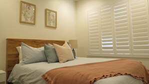 Un dormitorio con cabecera de madera, cama con varios almohadones, manta marrón y dos cuadros florales enmarcados en la pared.