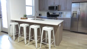Una cocina moderna con una isla central, taburetes de bar, un refrigerador de acero inoxidable y armarios de madera.