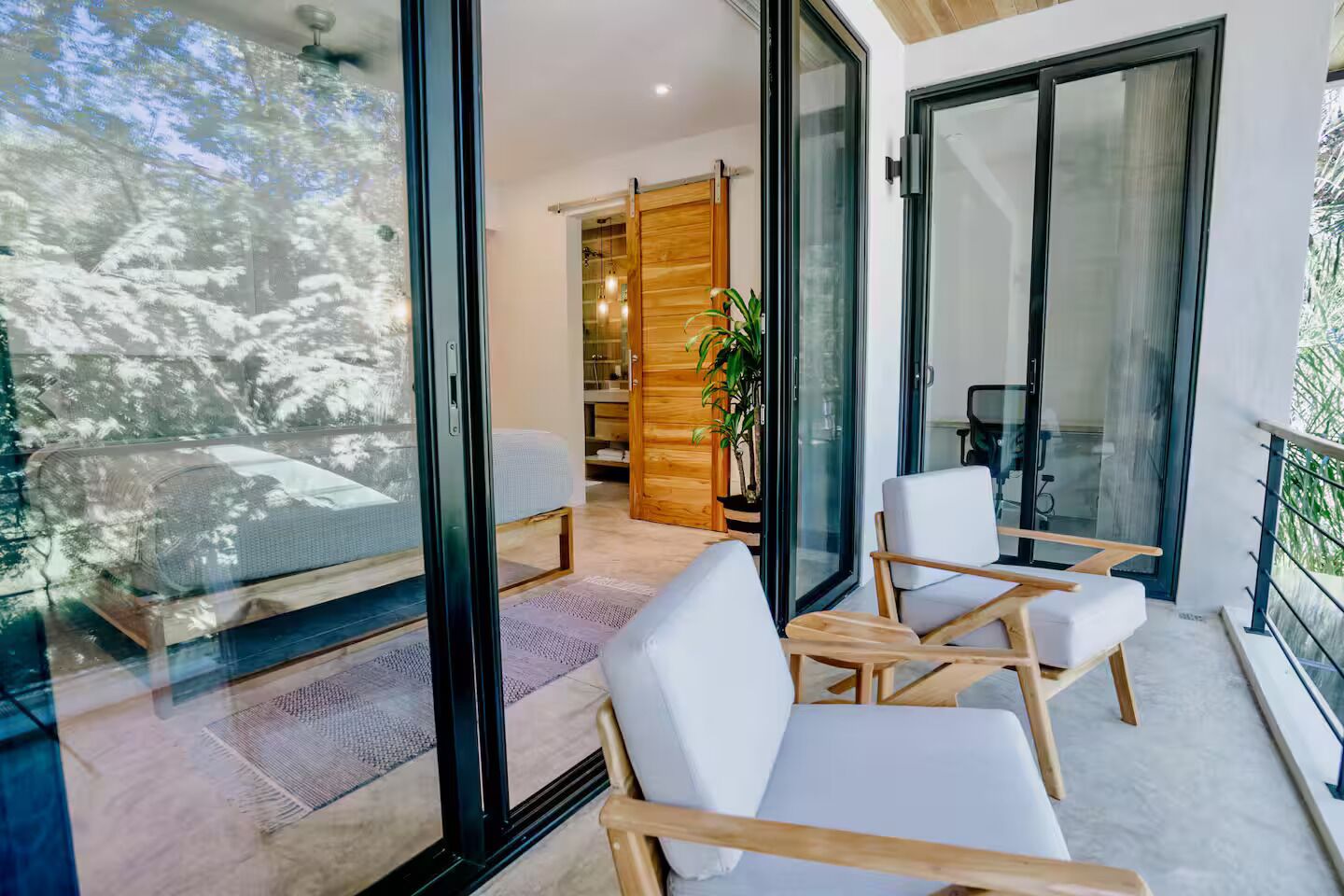 A modern room with a balcony, a sliding door leading to a wooden interior, and a view of trees outside.