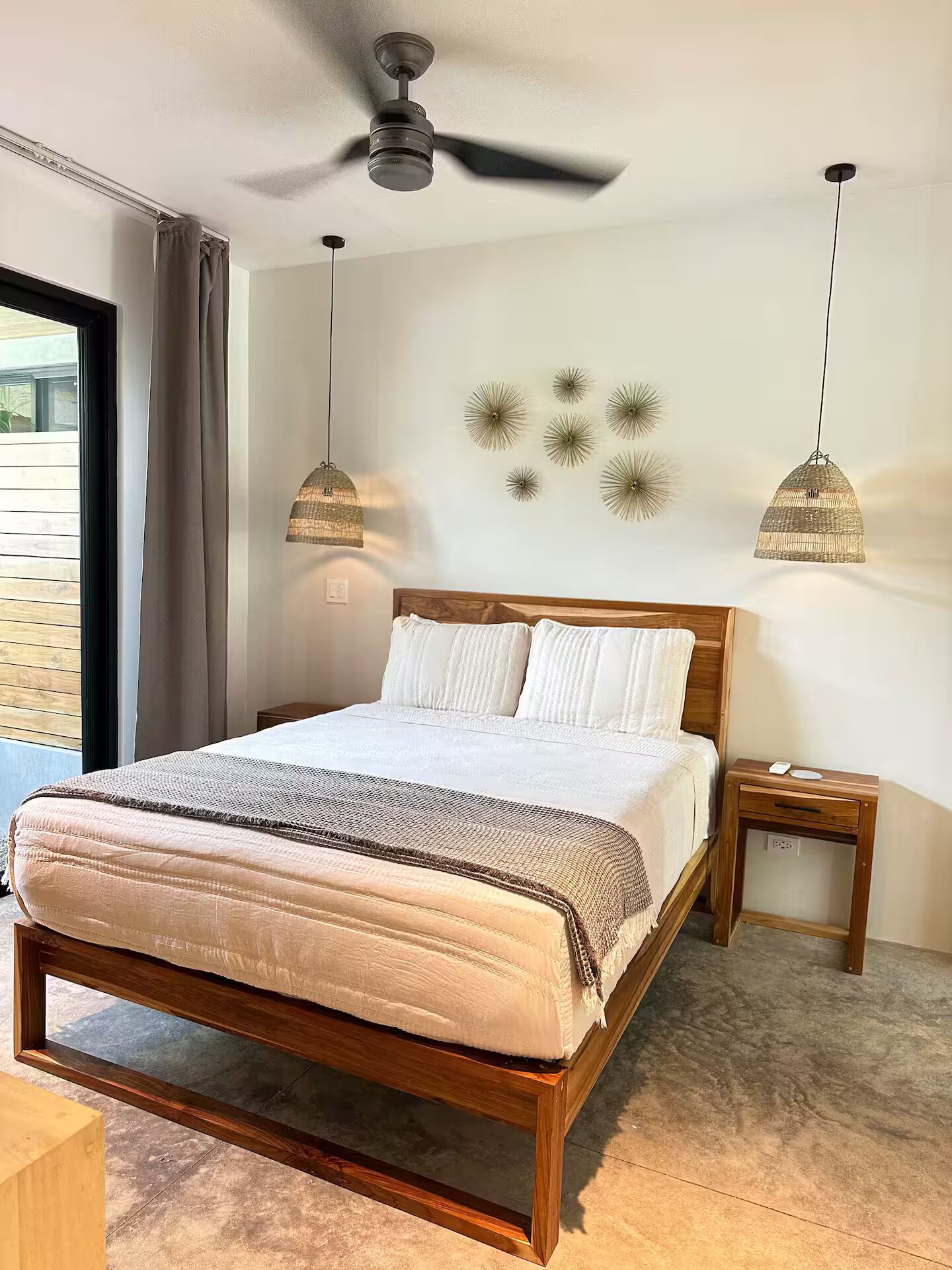 Un dormitorio con una cama de madera, un ventilador de techo, dos lámparas colgantes y un aplique de pared.