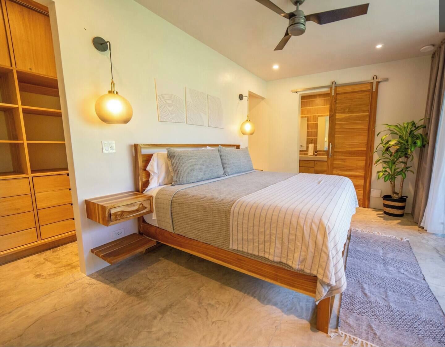 Ein Schlafzimmer mit einem hölzernen Bett, einem Deckenventilator, einer Wandleuchte, einem Kleiderschrank und einer Topfpflanze.