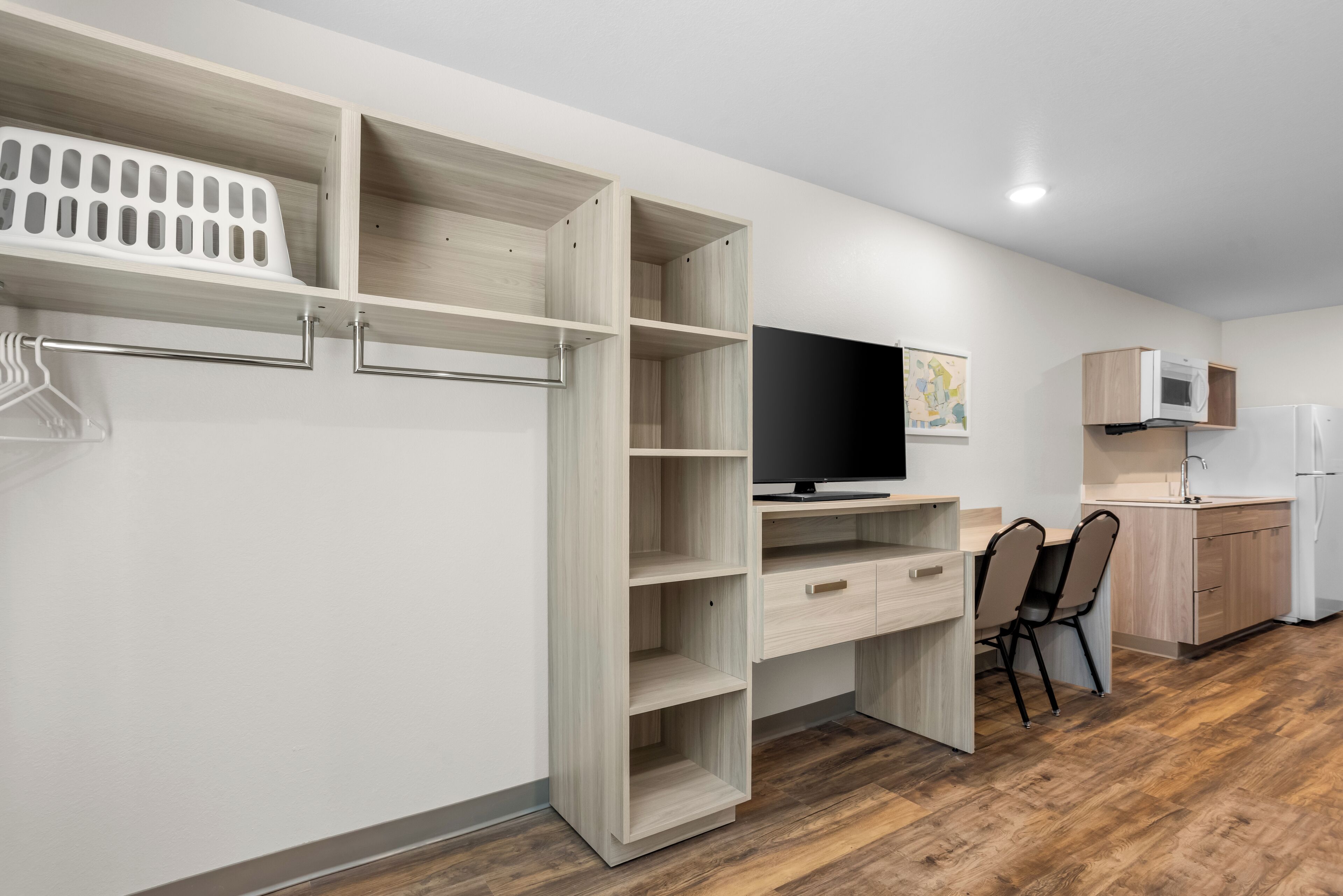 Una cocina compacta con televisión integrada, armarios de madera y un comedor con sillas.
