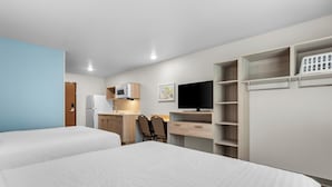 Ein Hotelzimmer mit zwei Betten, einer Küchenzeile, einem Fernseher und einem Kleiderschrank.