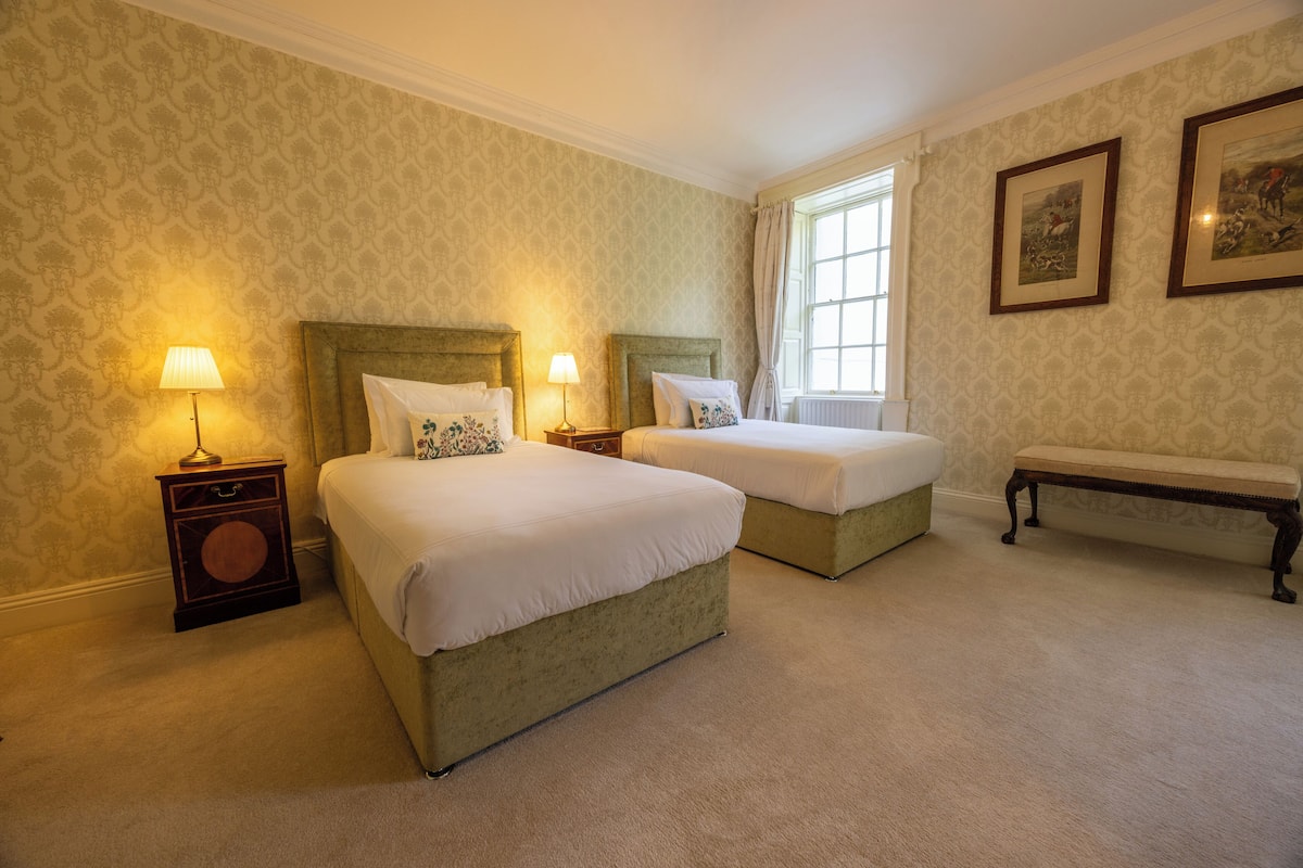 A hotel room with two beds, a bench, and a window with curtains.