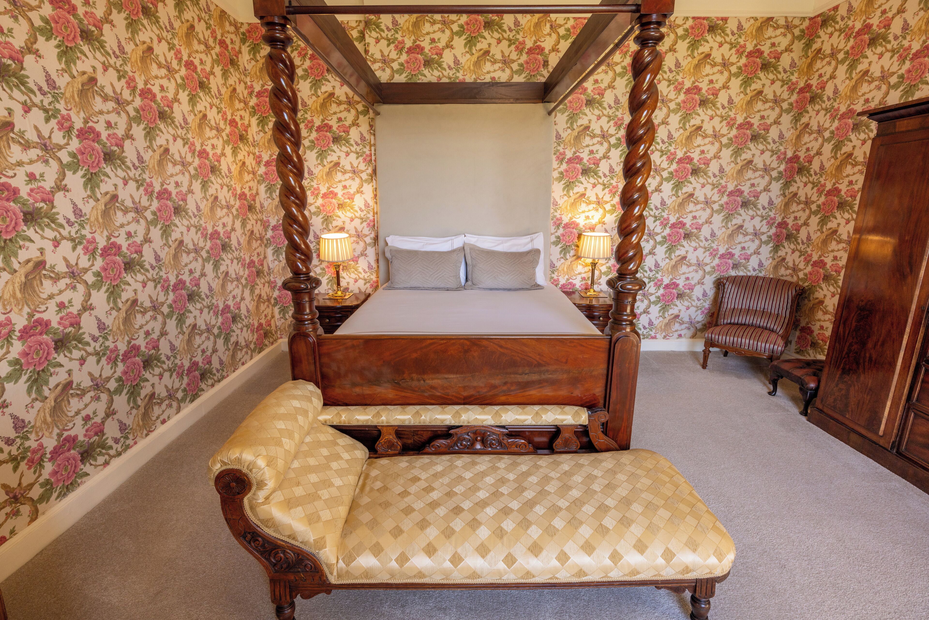 A four-poster bed with a canopy, a bench, and two bedside lamps.