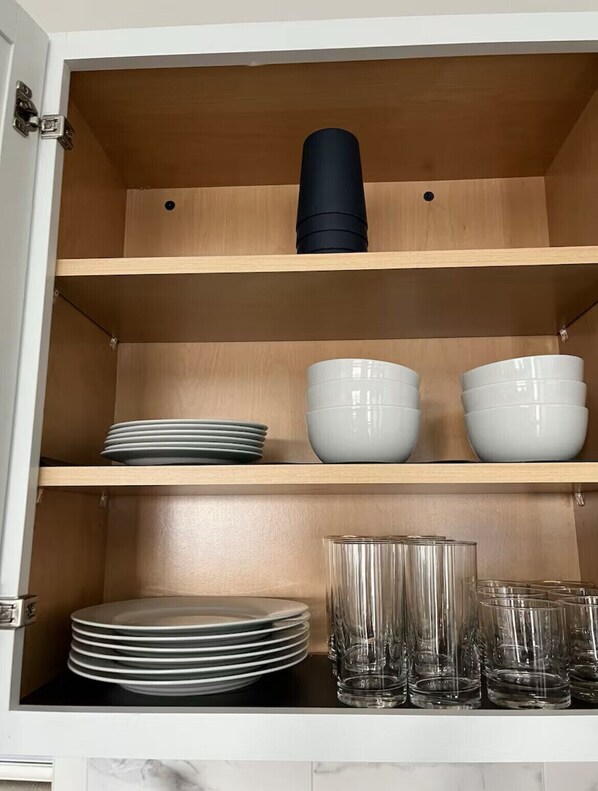 Un armario de cocina con repisas que contienen platos, tazones y cristalería.