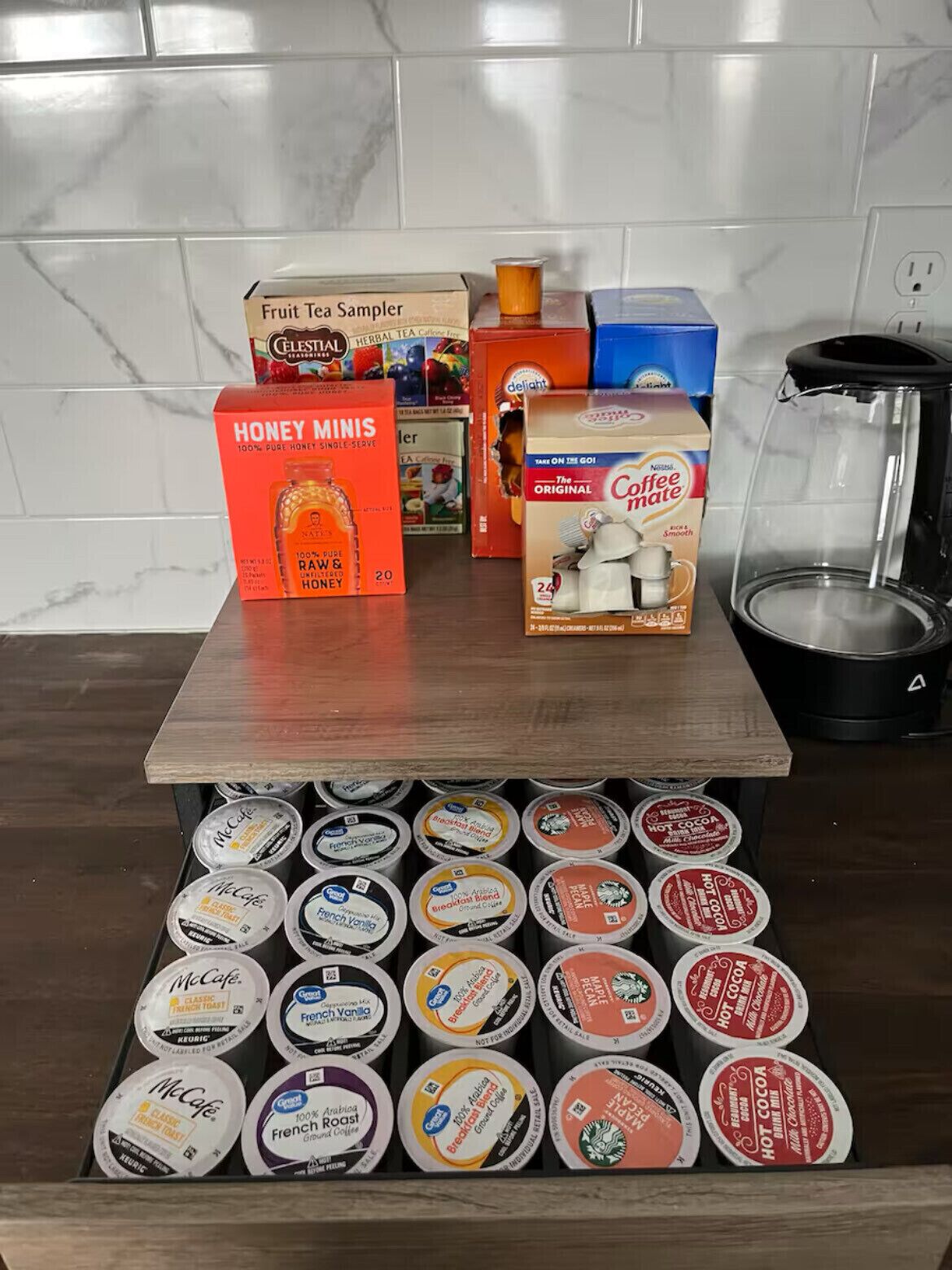 Una encimera de cocina con diversos productos de café y té, incluyendo una selección de té de frutas, mieles pequeñas y Coffee Mate.