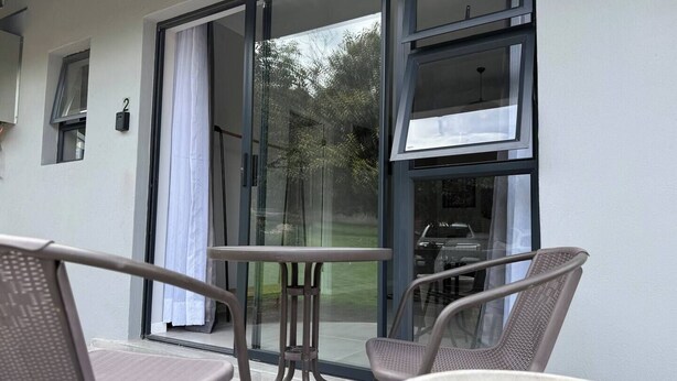 Ein Balkon mit zwei Stühlen, einem kleinen Tisch, großen Schiebeglastüren und Blick auf einen Garten.