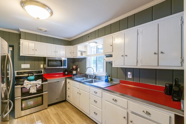 A kitchen with white cabinets, stainless steel appliances, a red countertop, and a window providing natural light. - Waterfront home on Mill Creek-5BR-3bath-Hot tub, Kayaks & private dock (Lusby)