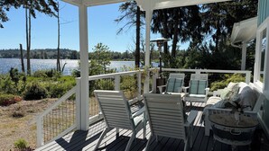 A covered deck with outdoor furniture, a view of a lake, and surrounding greenery.