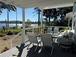 A covered deck with outdoor furniture, a view of a lake, and surrounding greenery.