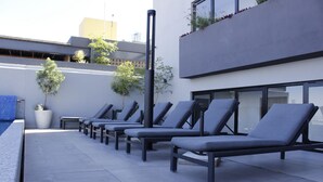 A row of lounge chairs aligned along a poolside, with a potted plant and a small table nearby. - Loft Pool Loft in Chapultepec (Guadalajara)