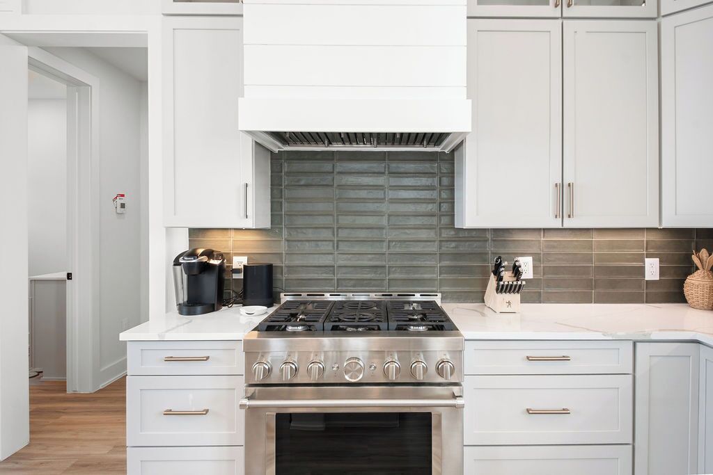 Une cuisine moderne dotée d’une cuisinière en acier inoxydable, de meubles blancs et d’un pare-feu gris.