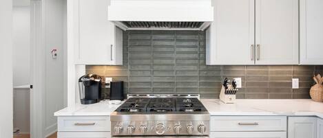 Une cuisine moderne dotée d’une cuisinière en acier inoxydable, de meubles blancs et d’un pare-feu gris.