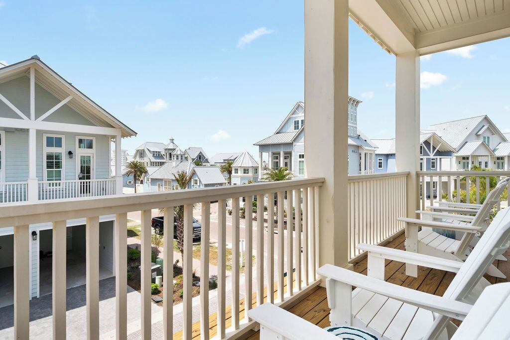 A balcony with white railings and chairs, overlooking a residential area with similar houses.