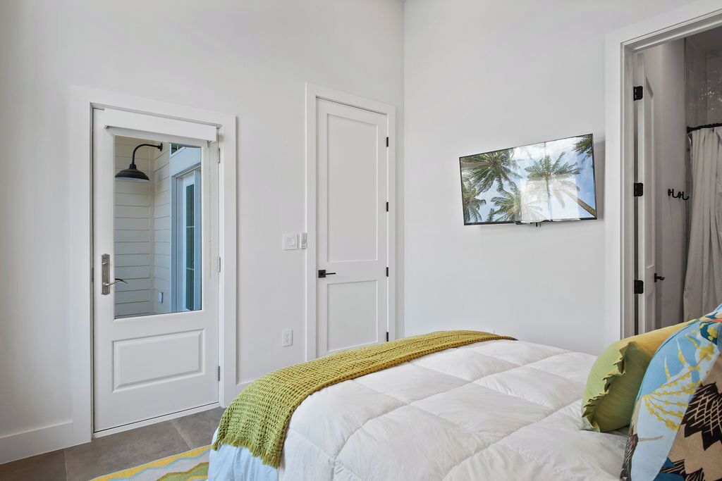 Un dormitorio con cama, una puerta, un televisor instalado en la pared y una puerta con panel de vidrio.