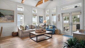 Un salon spacieux avec un plafond haut, des poutres apparentes, un ventilateur de plafond et de grandes fenêtres.