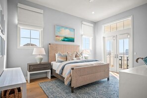 A bedroom with a bed, bedside tables, a painting, and a view through a glass door. - Sweet Retreat 405 RET (Port Aransas)