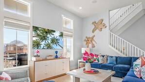 A spacious living room with a large window, a blue sofa, a white coffee table, and a staircase. - Sweet Retreat 405 RET (Port Aransas)