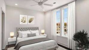 Ein Schlafzimmer mit einem gepolsterten Kopfteil, einem großen Bett, zwei Nachttischen mit Lampen, einem Deckenventilator und einem Fenster mit Vorhängen.