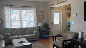 A living room with a grey sofa, a small table, a chair, and a lamp. There is a door with a window and a framed picture on the wall. - Spacious 5-bedroom house in beautiful Belmar w/ WiFi.  2 blocks from the beach! (Belmar)