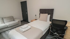 A hotel room with a bed, a desk, a chair, a sofa, and a door. - The Newborough Apartment 1 (Scarborough)