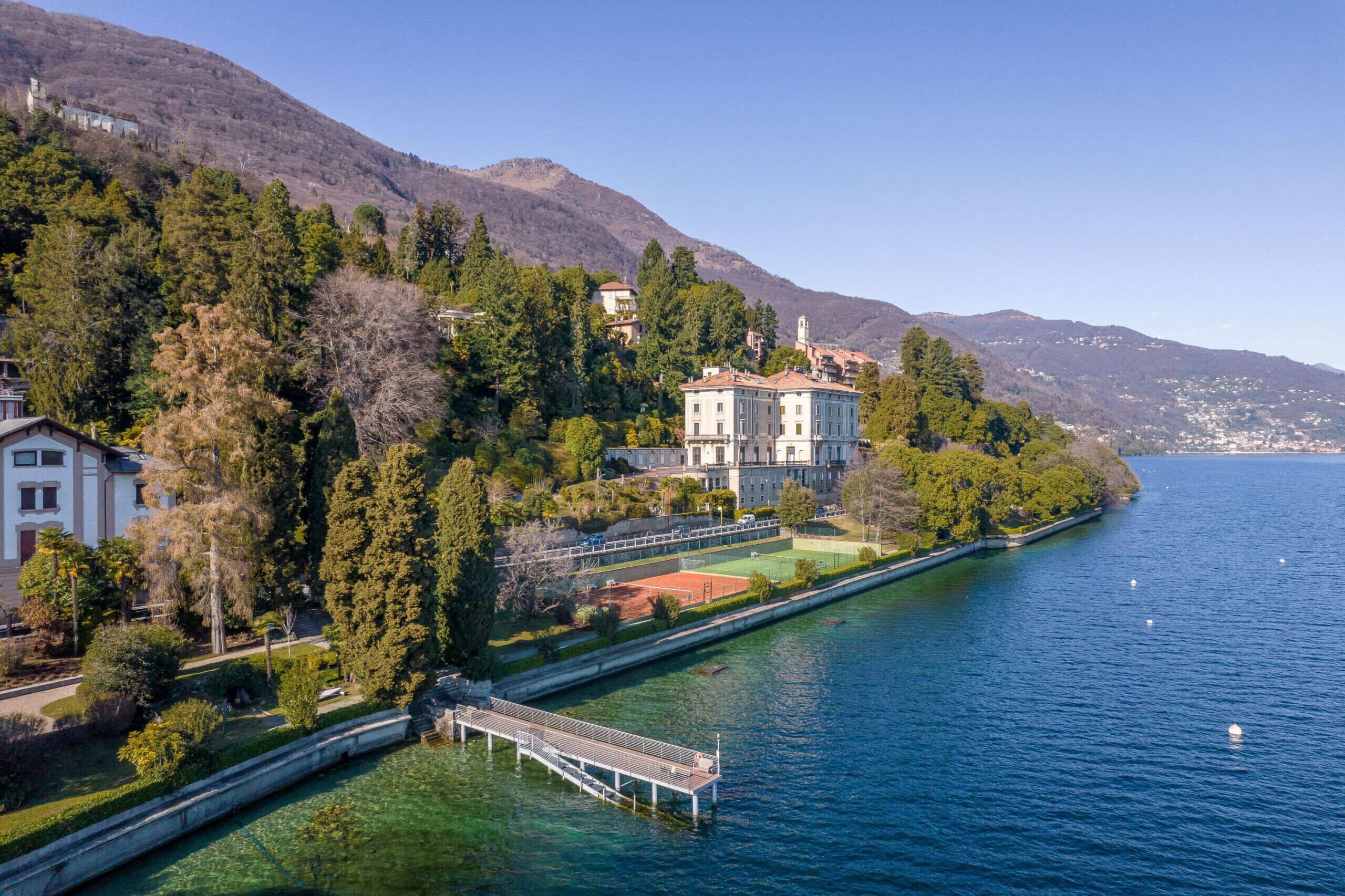 A lakeside property with a large building, a tennis court, and a dock.