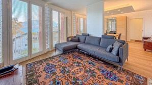 A modern living room with a grey sectional sofa, a patterned rug, and large windows with blinds. - Vera apartment with wonderful terrace lake view (Oggebbio)
