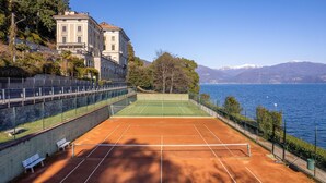 A tennis court with a net, benches, and a fence. - Vera apartment with wonderful terrace lake view (Oggebbio)