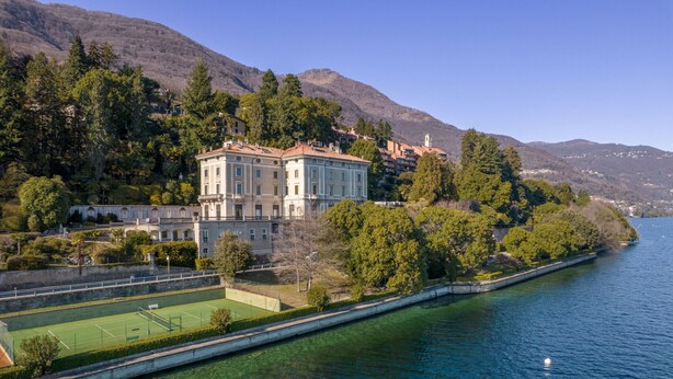 A large, historic building with a tennis court in front, surrounded by lush greenery and a calm lake. - Vera apartment with wonderful terrace lake view (Oggebbio)