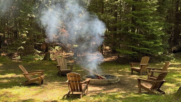 Una fogata rodeada de sillas Adirondack en un área boscosa.